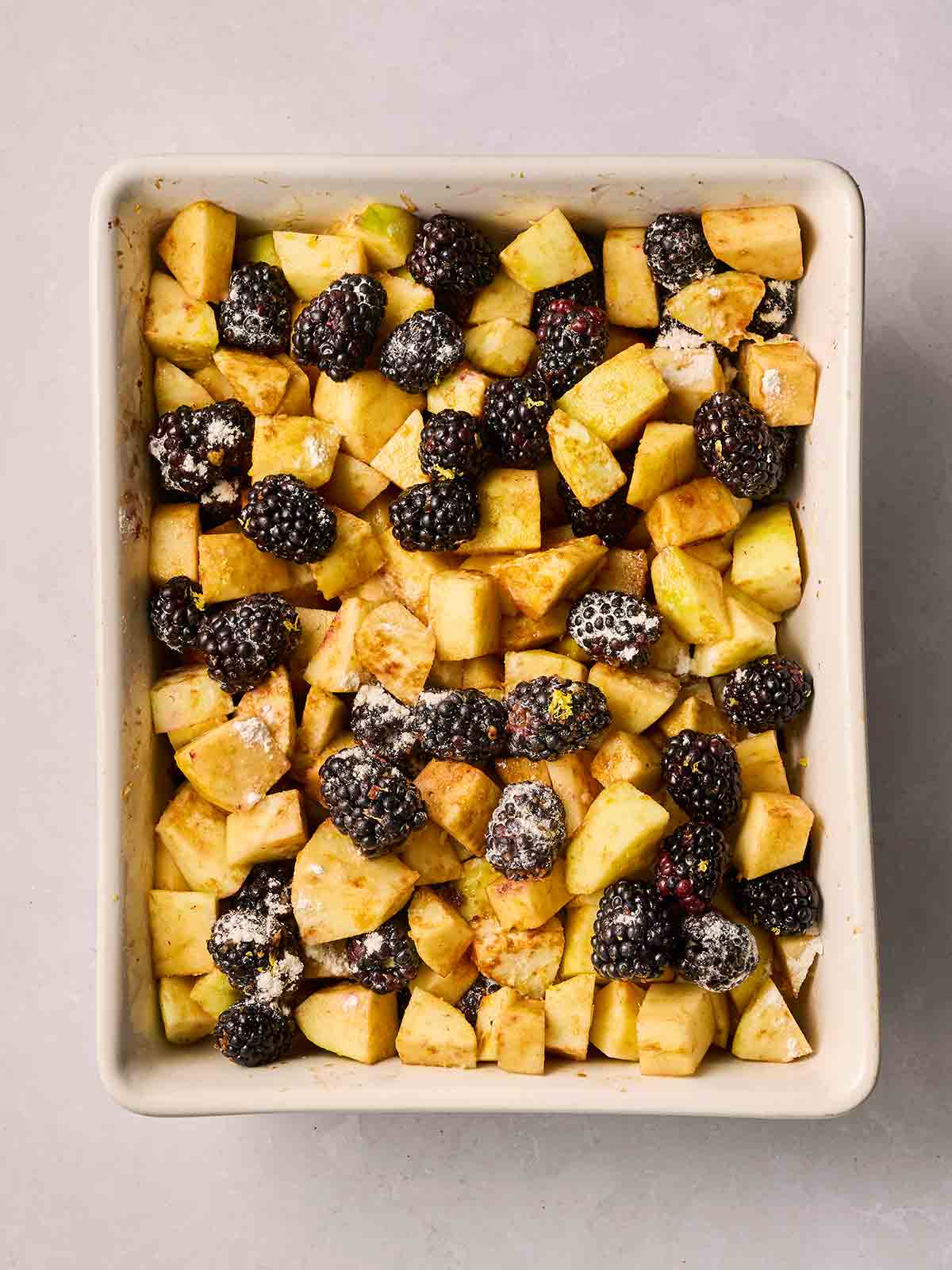 Chopped apple pieces and blackberries in a dish with sugar and flour on top.