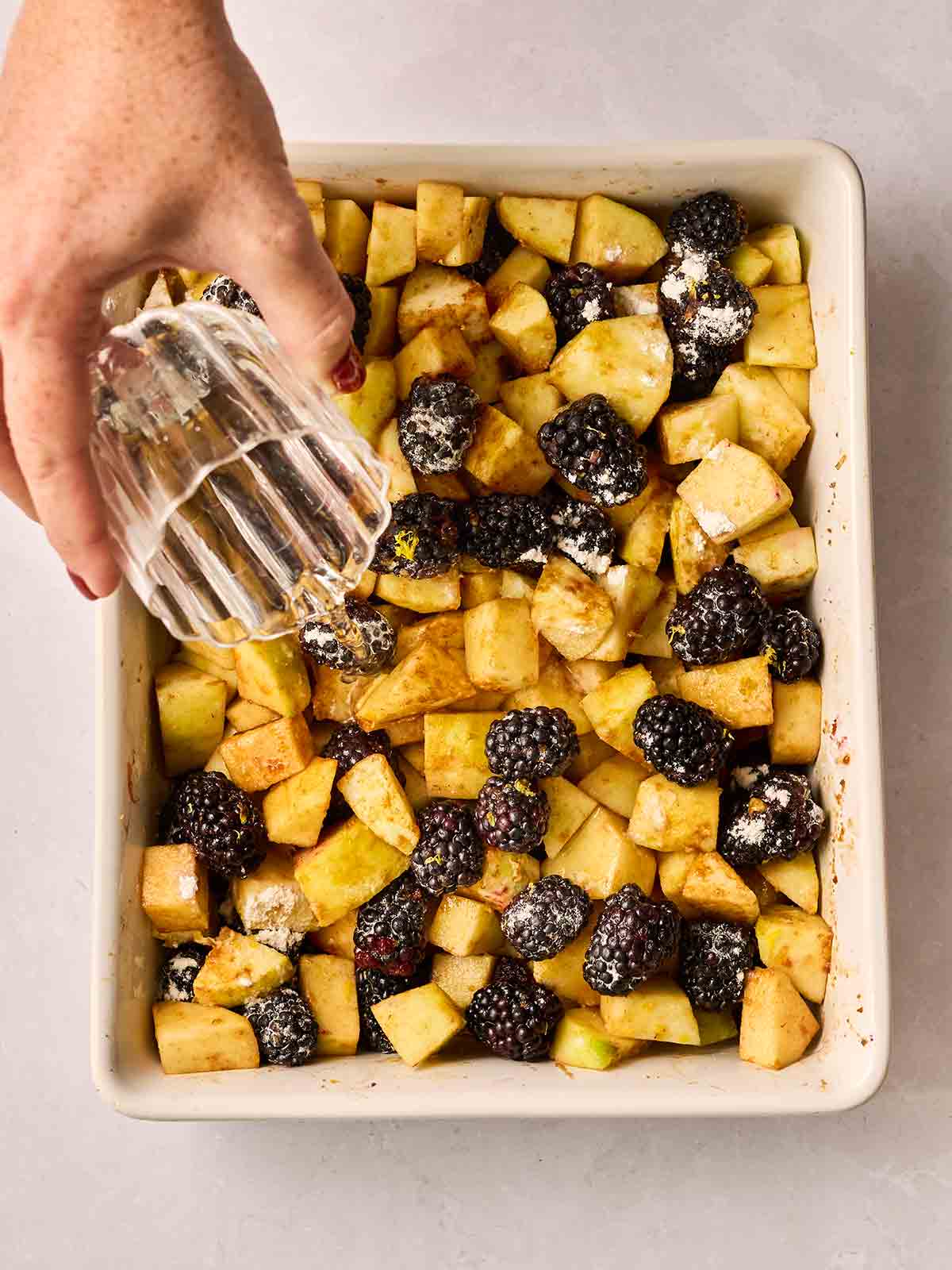 Apples and blackberries in a dish, with a hand pouring over a little water from a glass.