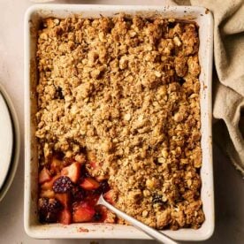 A dish filled with cooked Apple and Blackberry Crumble, with a spoon and a portion missing.