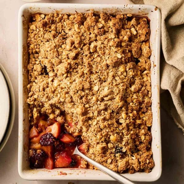 A dish filled with cooked Apple and Blackberry Crumble, with a spoon and a portion missing.