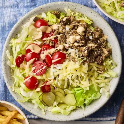 A plate of a cheeseburger-style salad, with minced beef, cheese, gherkins and lettuce.