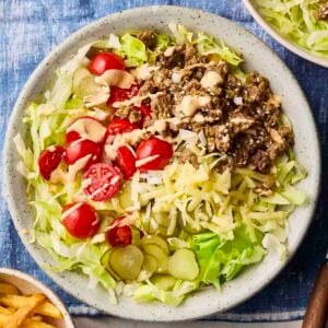 A plate of Big Mac Salad, with a blue table cloth and side of chips. With ground beef, cheese, pickles, tomatoes and lettuce.