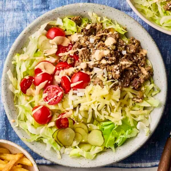 A plate of Big Mac Salad, with a blue table cloth and side of chips. With ground beef, cheese, pickles, tomatoes and lettuce.