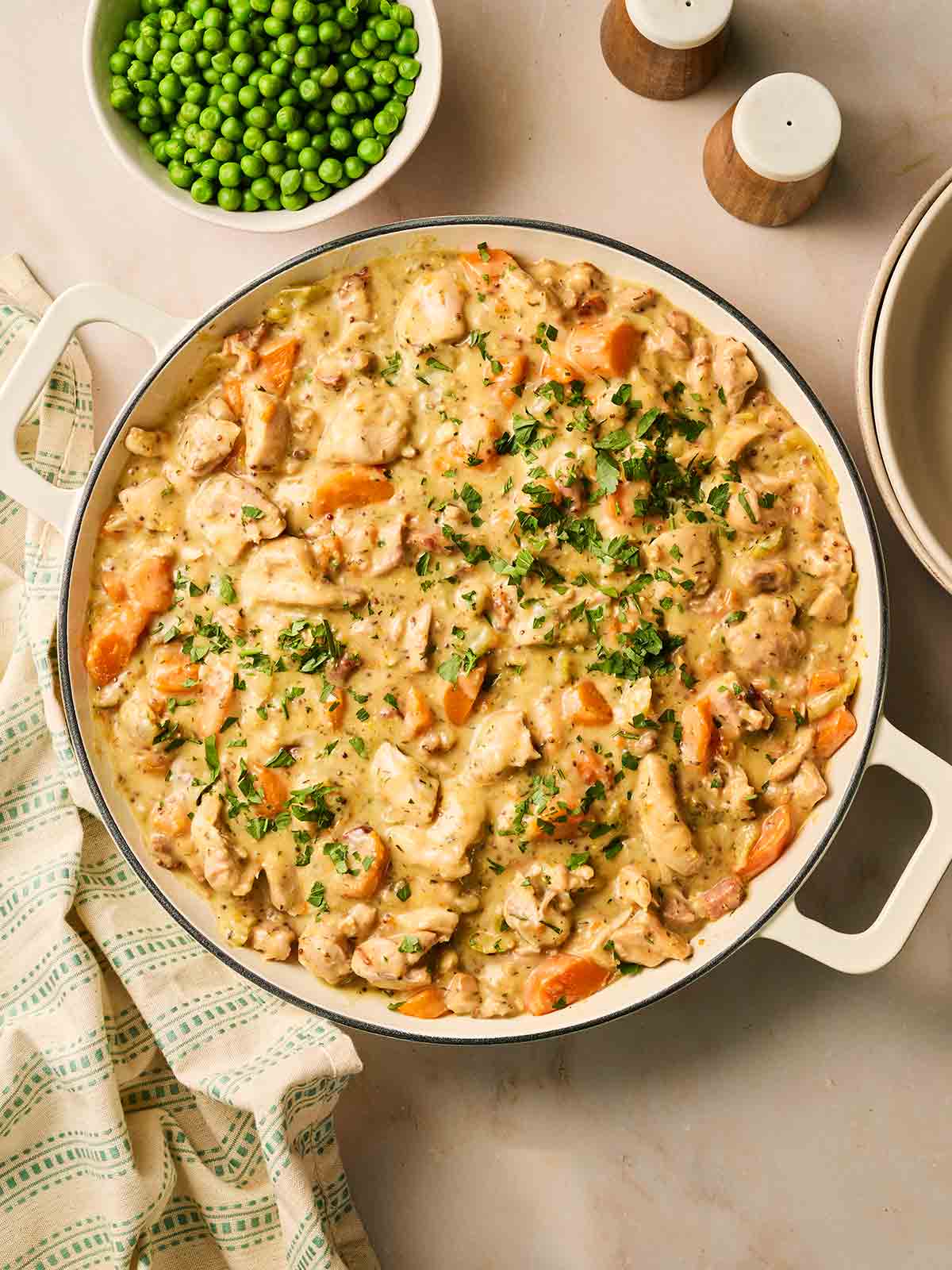 A pan filled with chicken casserole, ready to serve with a bowl of peas to the side and salt and pepper.