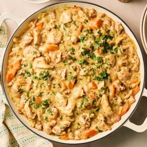 A large pan of casserole made with hciken, carrots and other veggies, with a bowl of peas to the side.