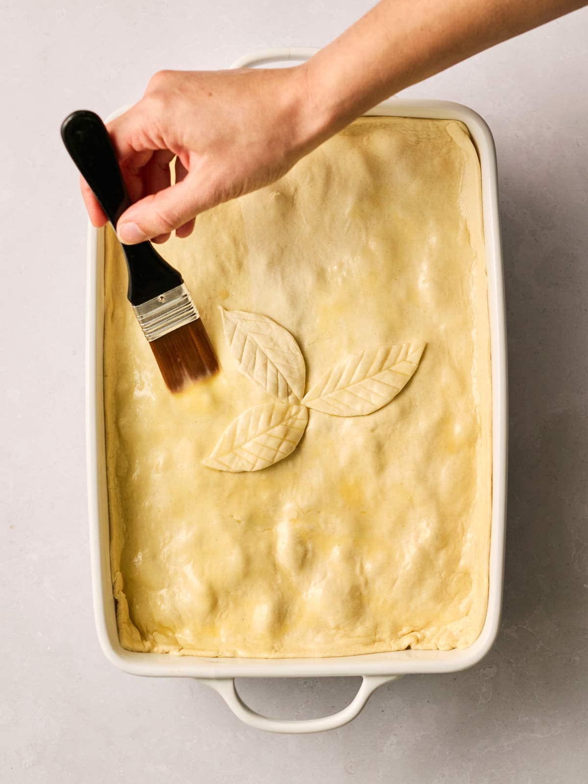 A uncooked Chicken & Mushroom Pie being brushed with egg, ready for the oven.