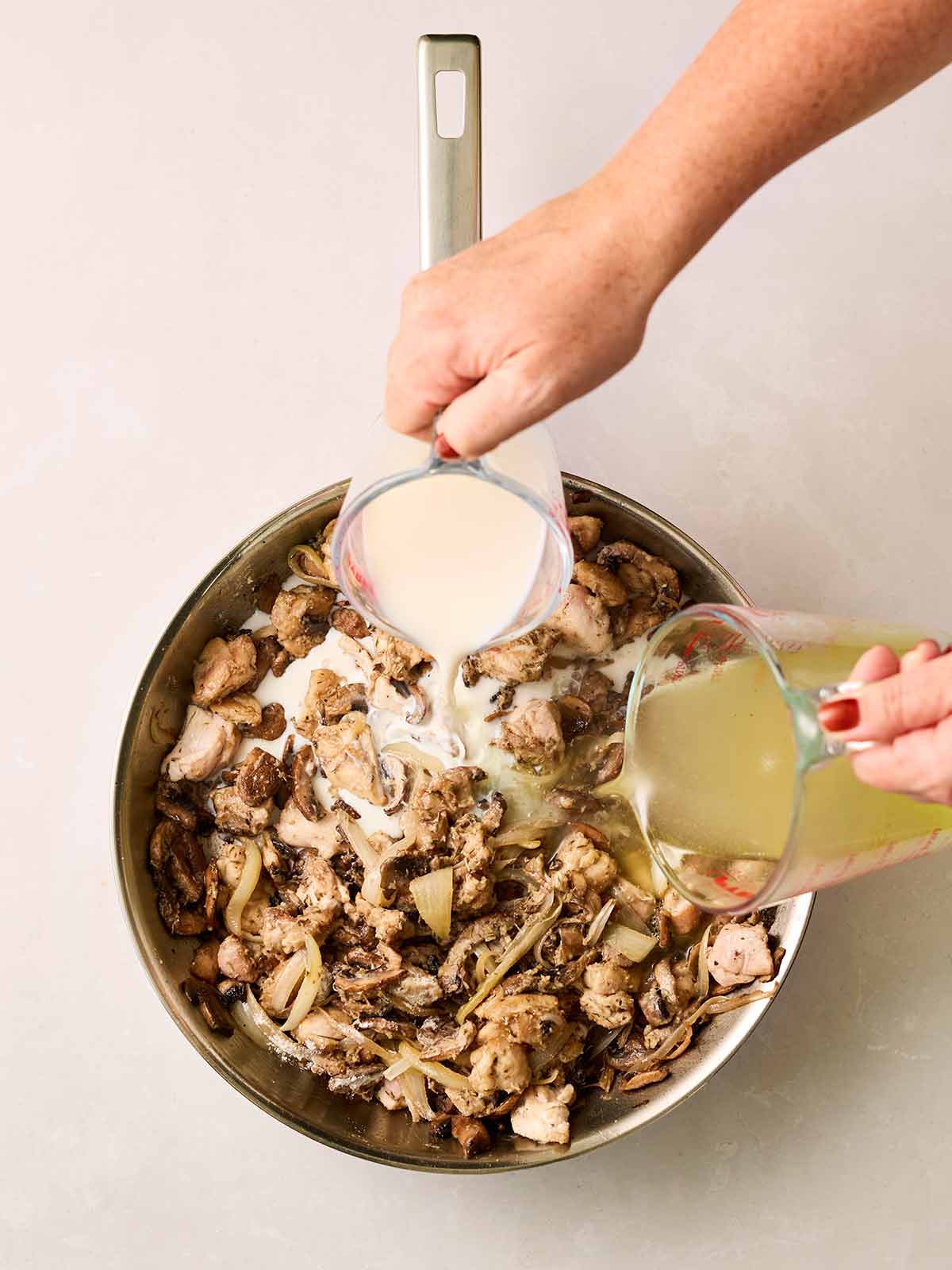 A pan filled with chicken and mushroom with stock and milk being poured in.