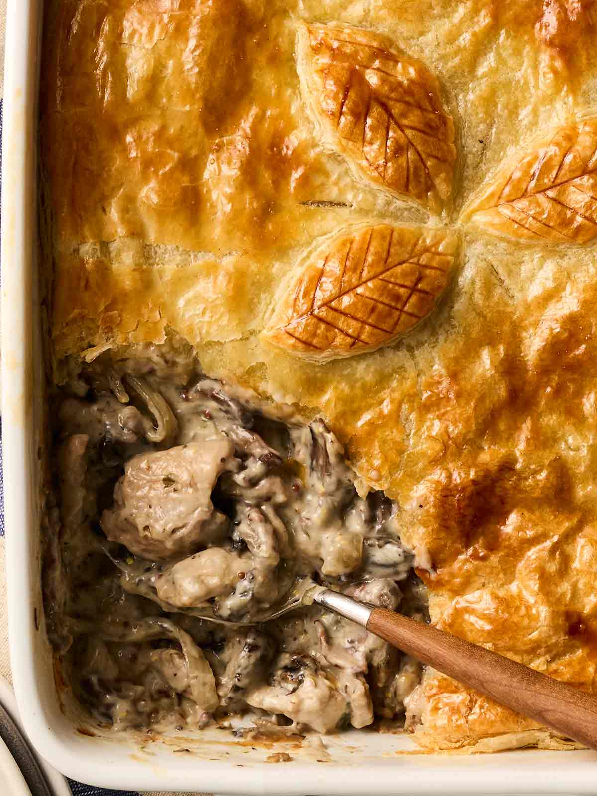 A golden crusted pie with a Chicken and mushroom pie filling, with a spoon about to serve.