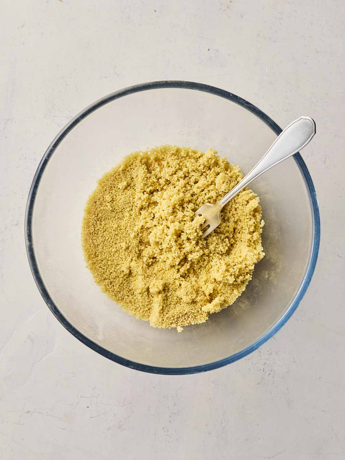 A glass bowl with couscous inside, with a fork fluffing it up.
