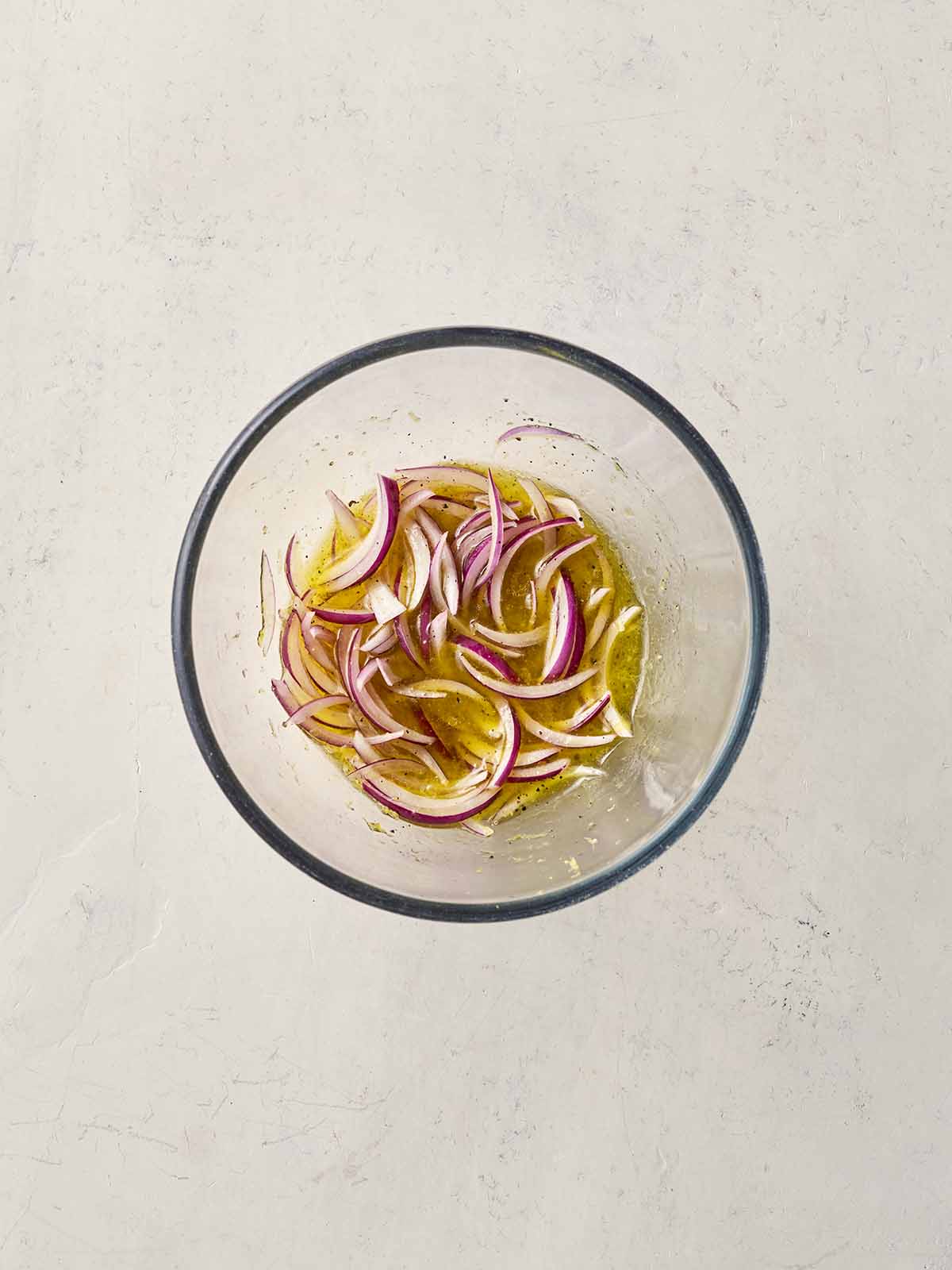 Sliced red onions in a glass bowl with a oil and lemon dressing.