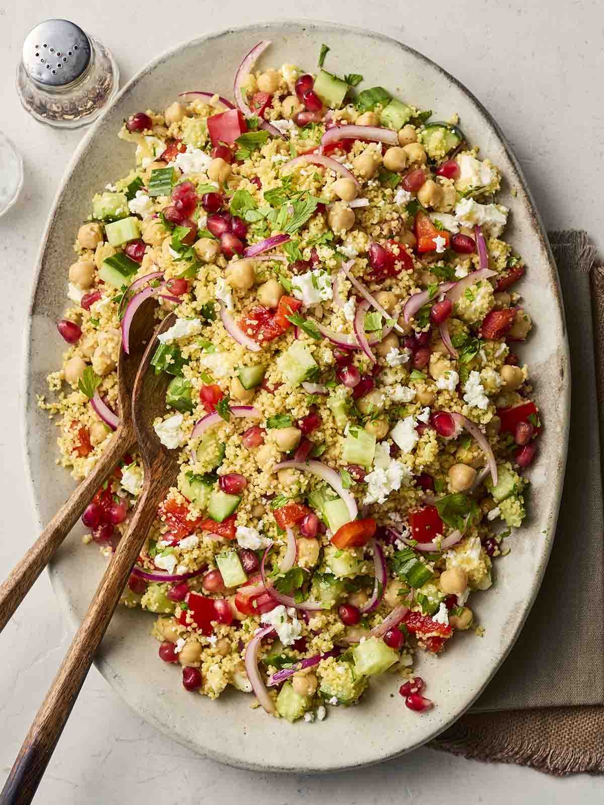 A plate of couscous salad, with chickpeas, onion, cucumber, pomegranate, pepper and parsley.
