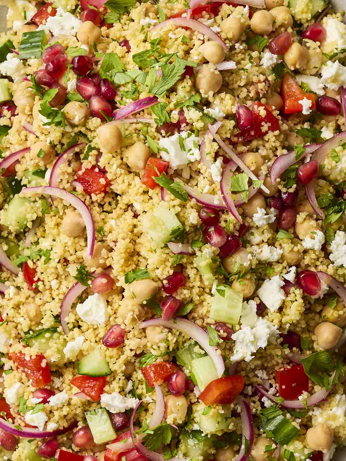 A close up of a salad with couscous and feta, chickpeas, pomegranate and onion, cucumber and pepper, for a colourful Mediterranean dish.
