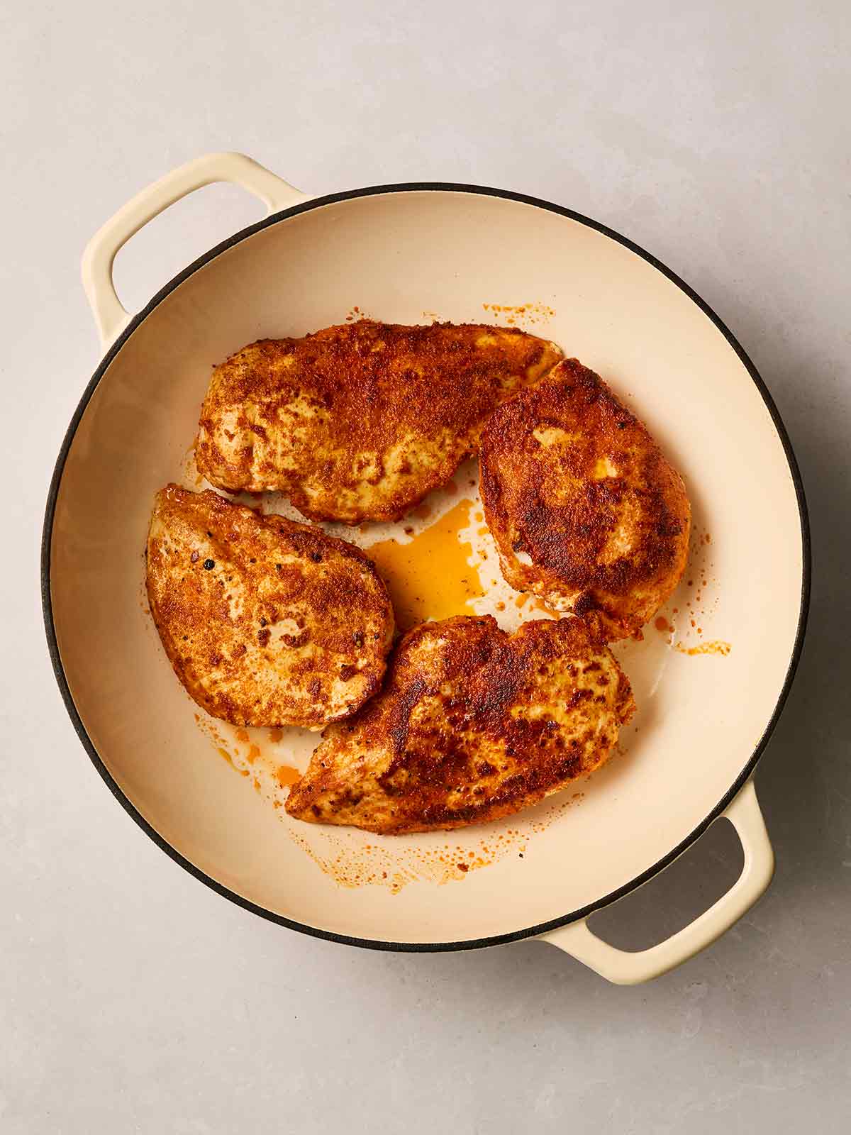 A pan filled with cooked chicken breasts with a red paprika coating.