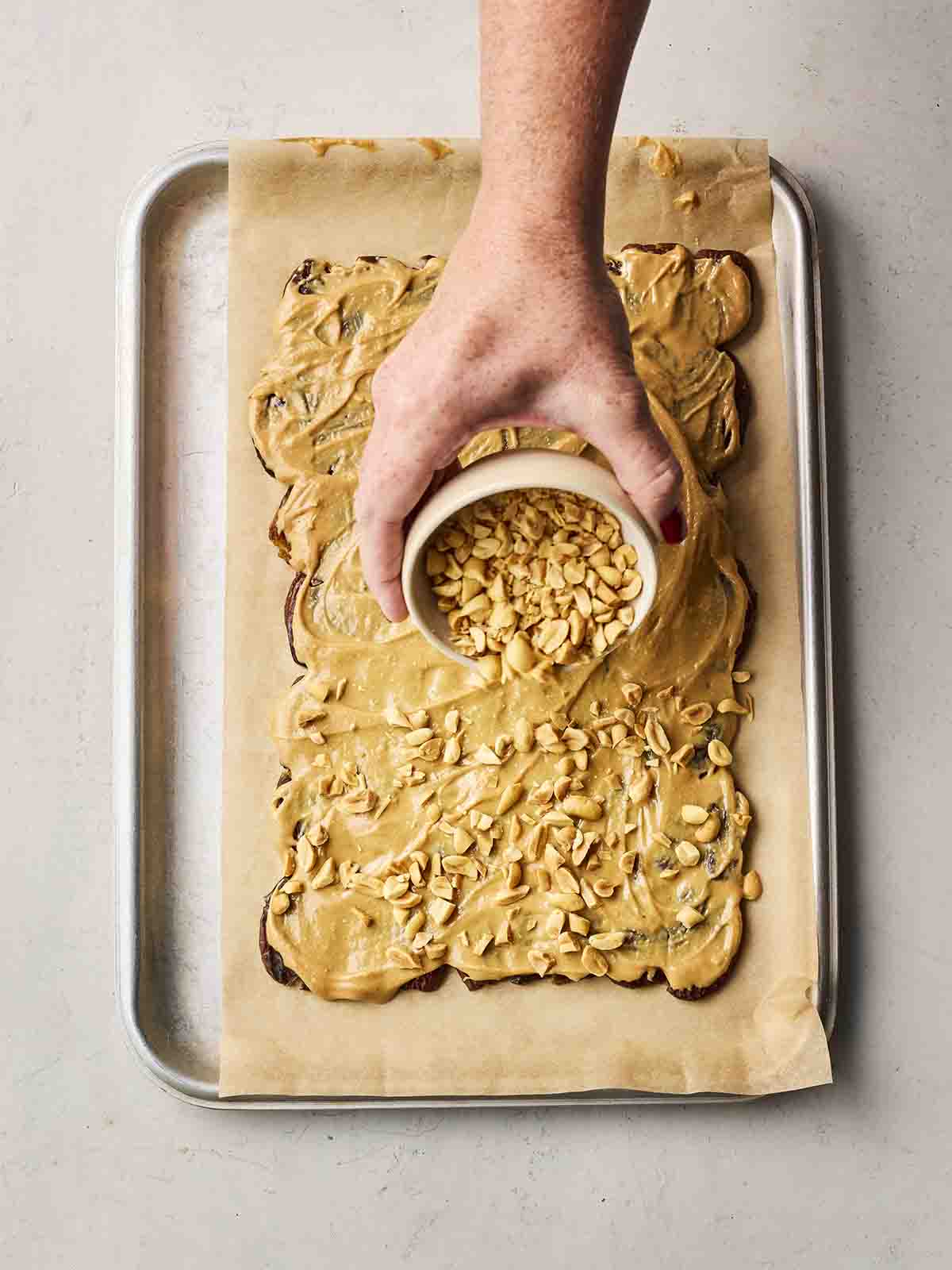 A hand spreading over peanuts on top of dark bark with peanut butter.