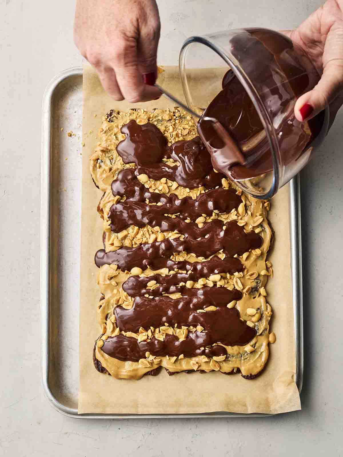 Two hands pouring melted chocolate over peanut butter-covered dates.