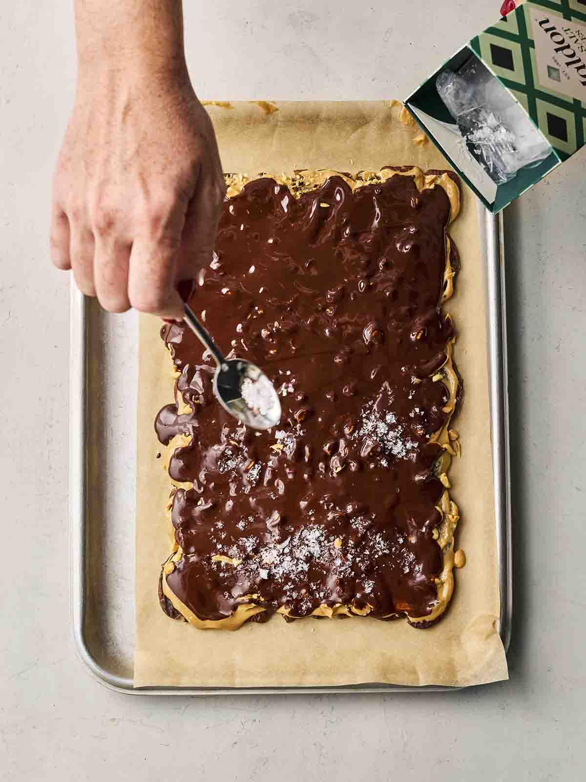 A hand spreading sea salt over chocolate covered dates and peanut butter.