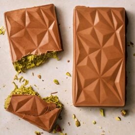 Two homemade bars of Dubai Chocolate side by side, one of them broken in the middle to show the green filing.