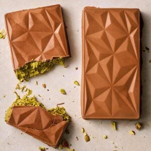 Two homemade bars of Dubai Chocolate side by side, one of them broken in the middle to show the green filing.