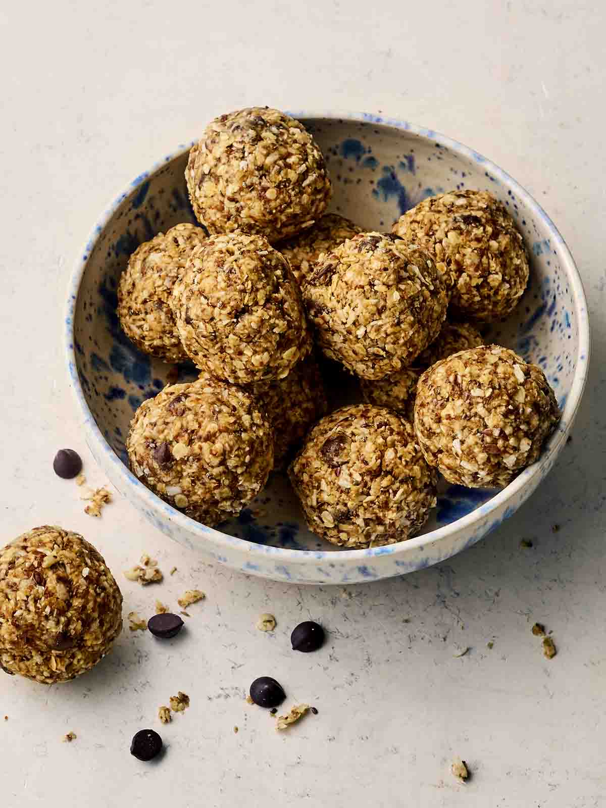 A bowl of round homemade energy balls, with one on a surface with chocolate chips.