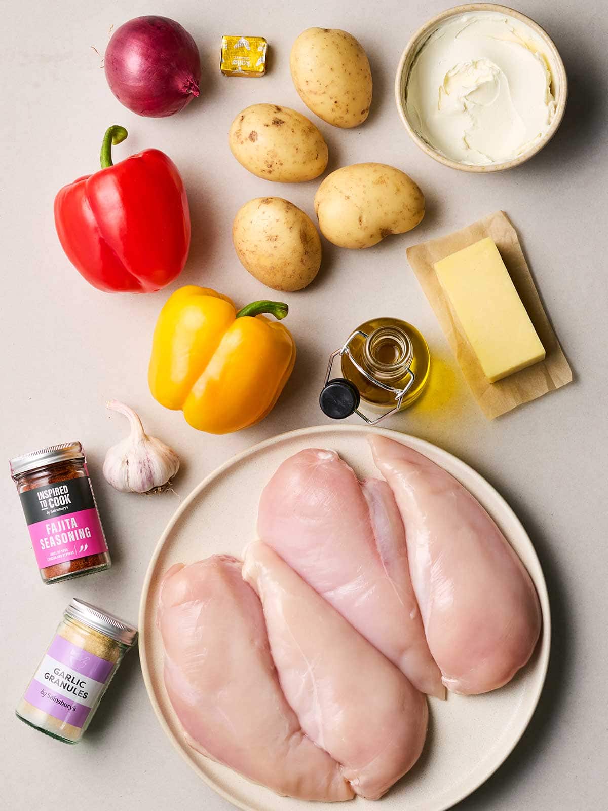 Ingredients laid out on a table, including raw chicken breast, pepper, potatoes and seasonings.