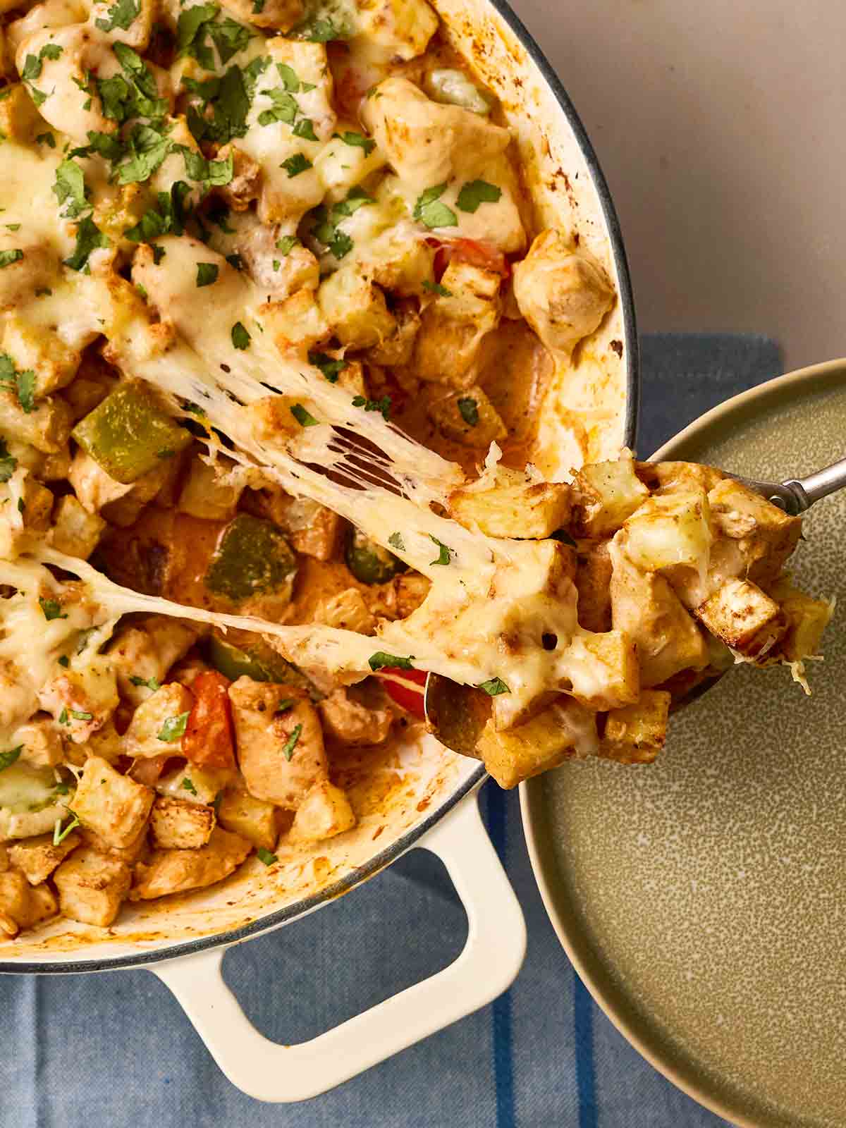 A pan filled with air fryer potatoes in a chicken fajita sauce, with a spoon dishing up onto a plate.