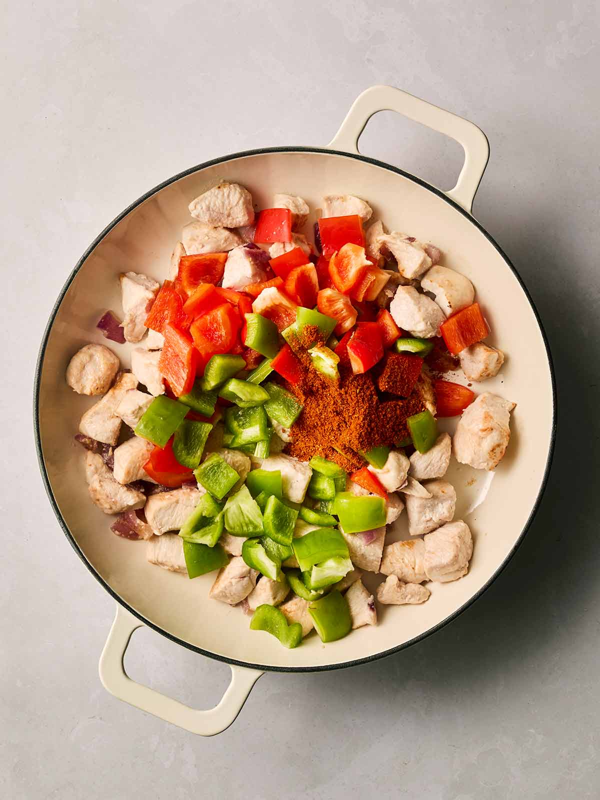 A pan filled with cooked chicken cubes and peppers and fajita seasoning.