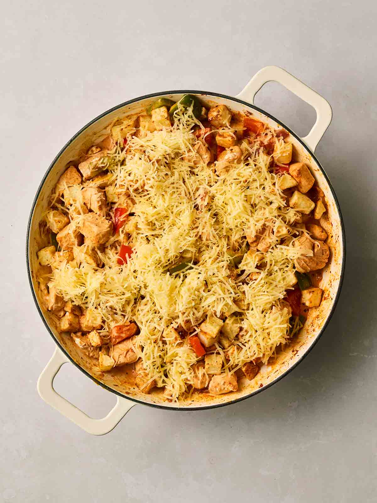 A pan filled with chicken fajita potatoes with grated cheese on top.
