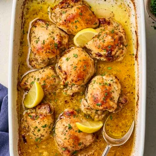 An oven dish with baked lemon chicken inside with a spoon to serve.