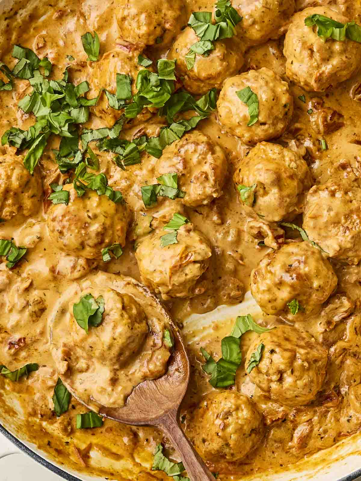 A creamy sauce with meatballs and a spoon.
