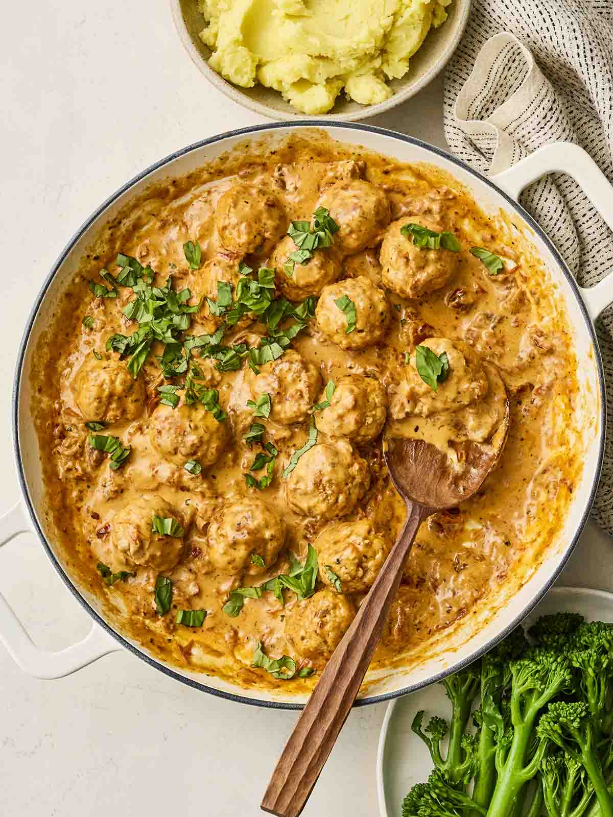A homemade meatballs sauce with cream in a pan with a spoon and mash to the side.