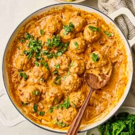 A white pan filled with Marry Me Chicken Meatballs, a creamy sauce and parsley over the top.