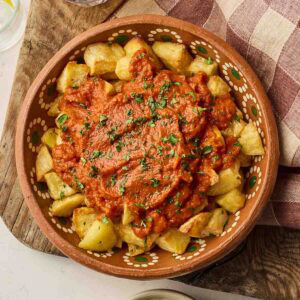 A clay dish fulled with potatoes and red tomato sauce for Patatas Bravas tapas dish.