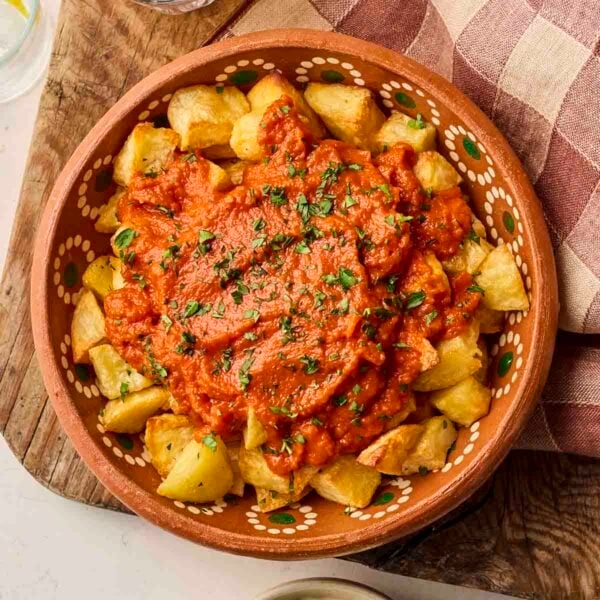 A clay dish fulled with potatoes and red tomato sauce for Patatas Bravas tapas dish.