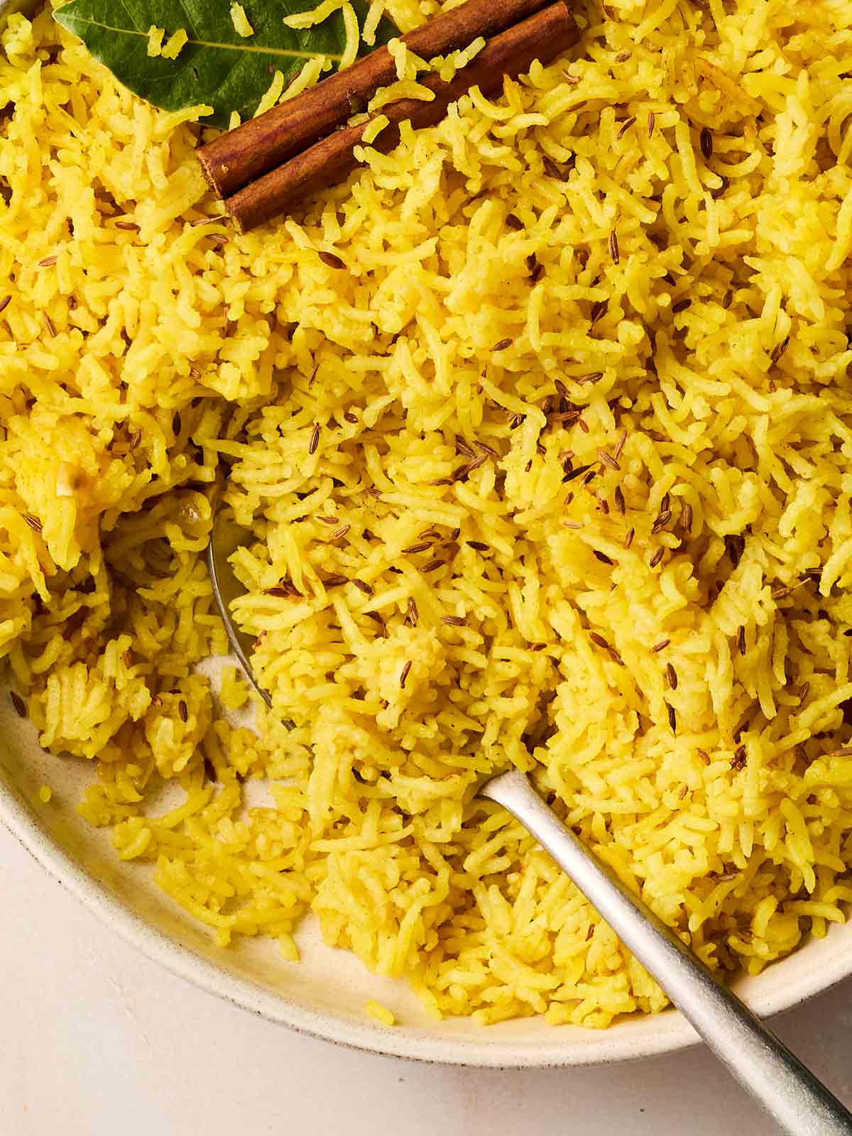 A close up of yellow Pilau Rice with a spoon stuck into it to serve.