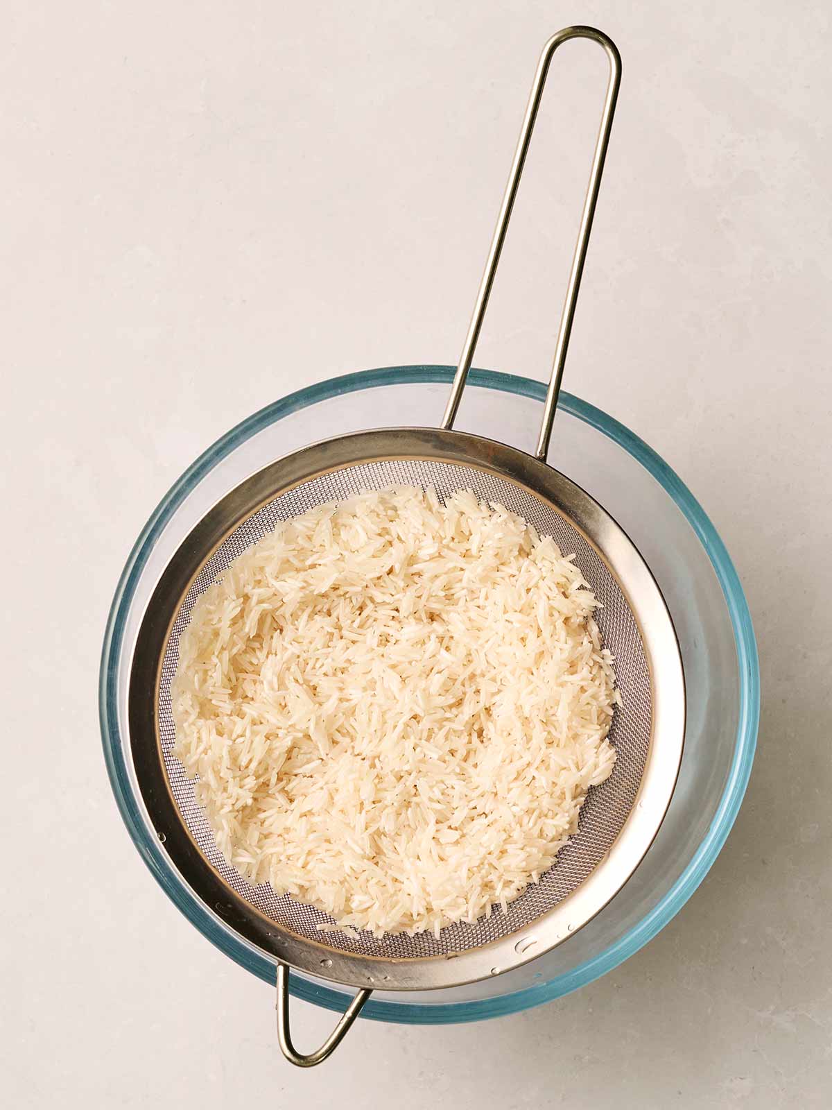 White rice in a sieve over a glass bowl.