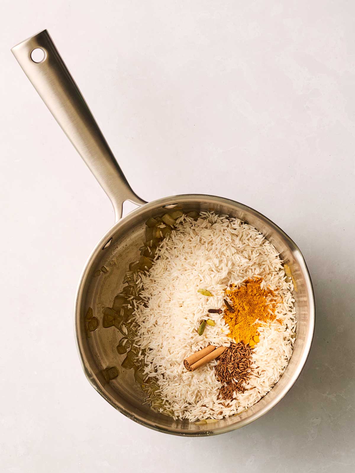 A pan with rice inside and lots of spices and a cinnamon stick.
