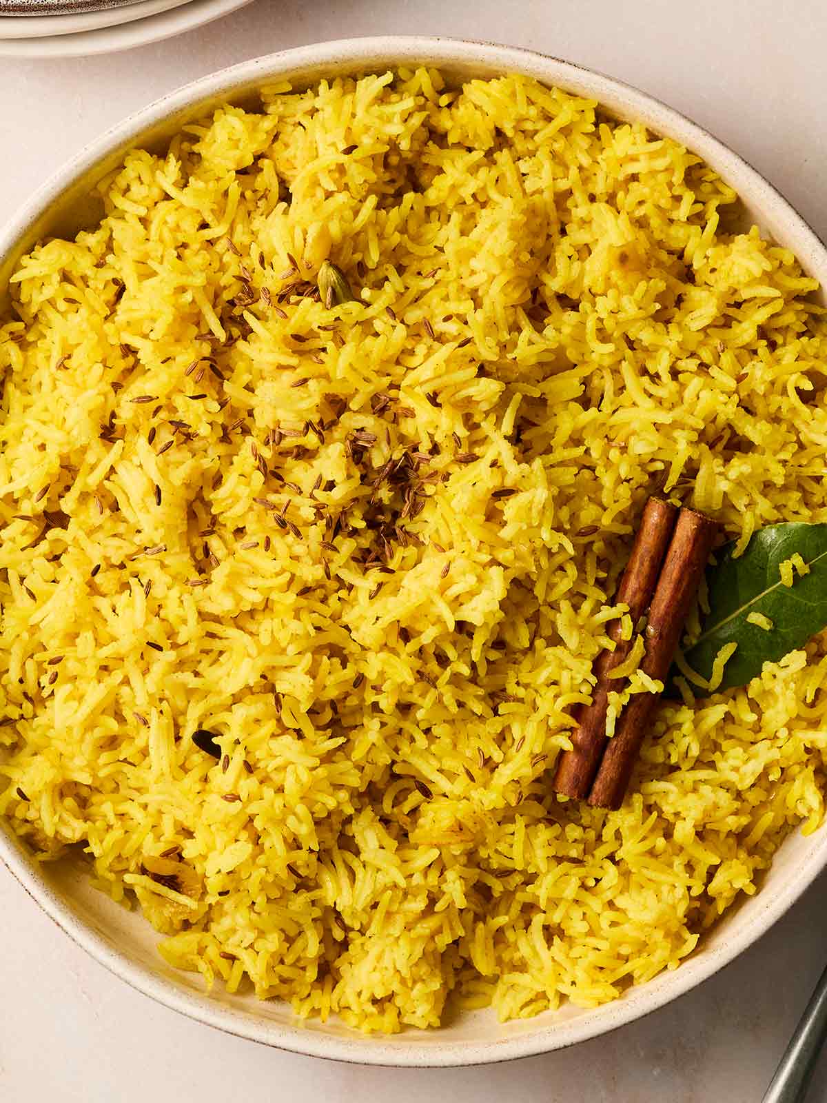 A large bowl filled with yellow Pilau Rice with a cinnamon stick and bay leaf in the top for decoration.