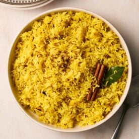 A white bowl filled with yellow Pilau Rice on a white surface.