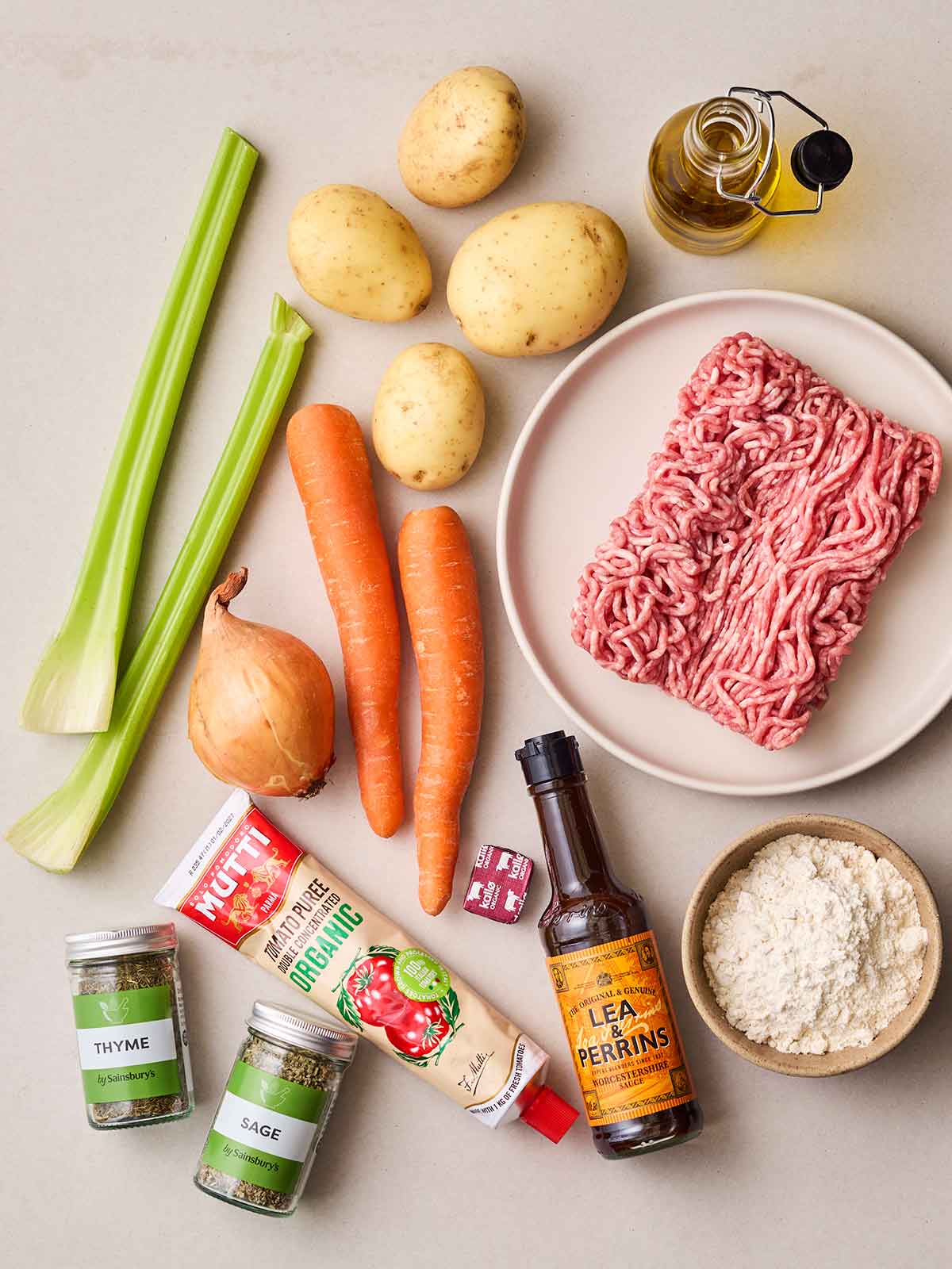 Raw ingredients laid out on a counter top for shepherd's pie, including mince, vegetables, tomato puree, herbs, Worcestershire sauce and flour.
