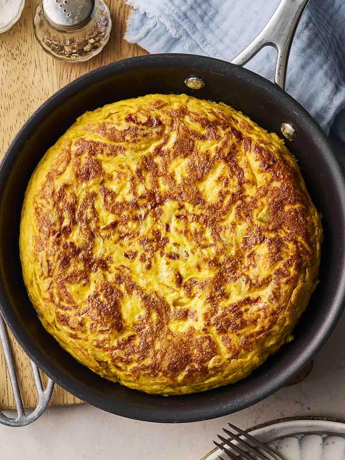 A pan with a Spanish Omelette inside, on a wooden table to serve.