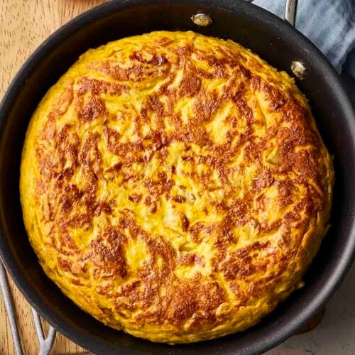 A Spanish Tortilla on a table in a black pan, ready to serve.