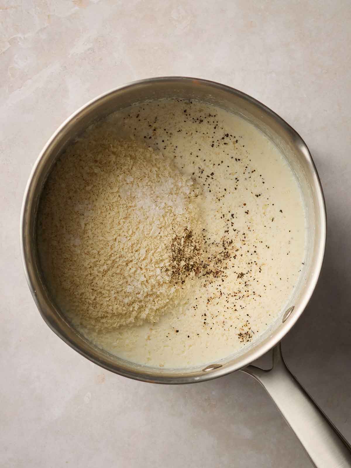 A pan of milk with breadcrumbs on top, ready to turn into Bread Sauce.
