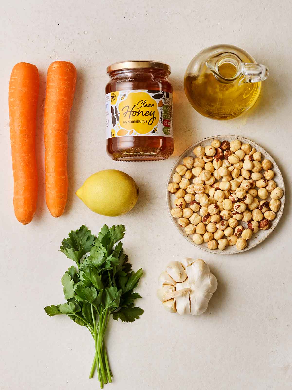 Ingredients laid out on a white counter, including carrots, honey, oil, chickpeas, garlic, lemon and parsley.