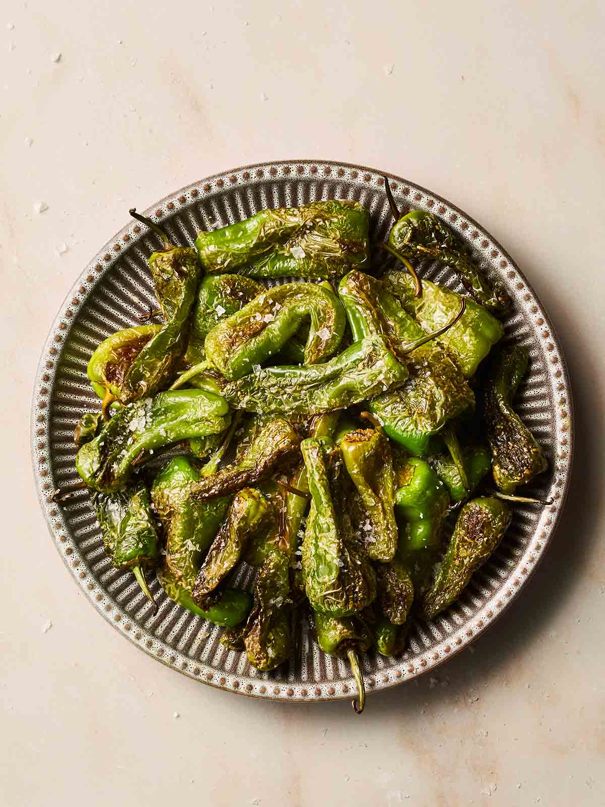 A stripy plate filled with roasted padron peppers.