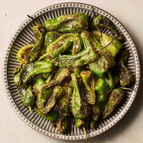 A close up of blisters, salted padron peppers on a stripy plate.