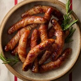 A close up of a dish of Pigs in Blankets decorated with sprigs of rosemary.