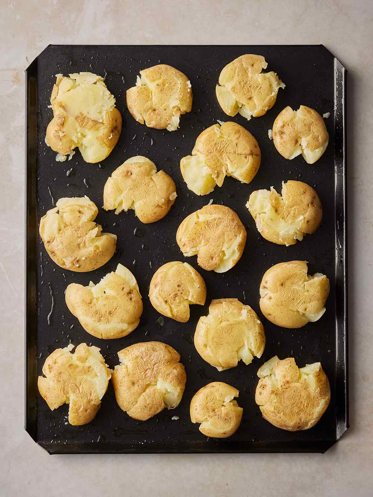 A baking tray filled with smashed potatoes, yet to be cooked.