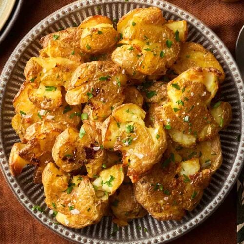 A batch of crushed potatoes with parsley and salt, on a stripy plate, on a brown tablecloth, ready to serve.