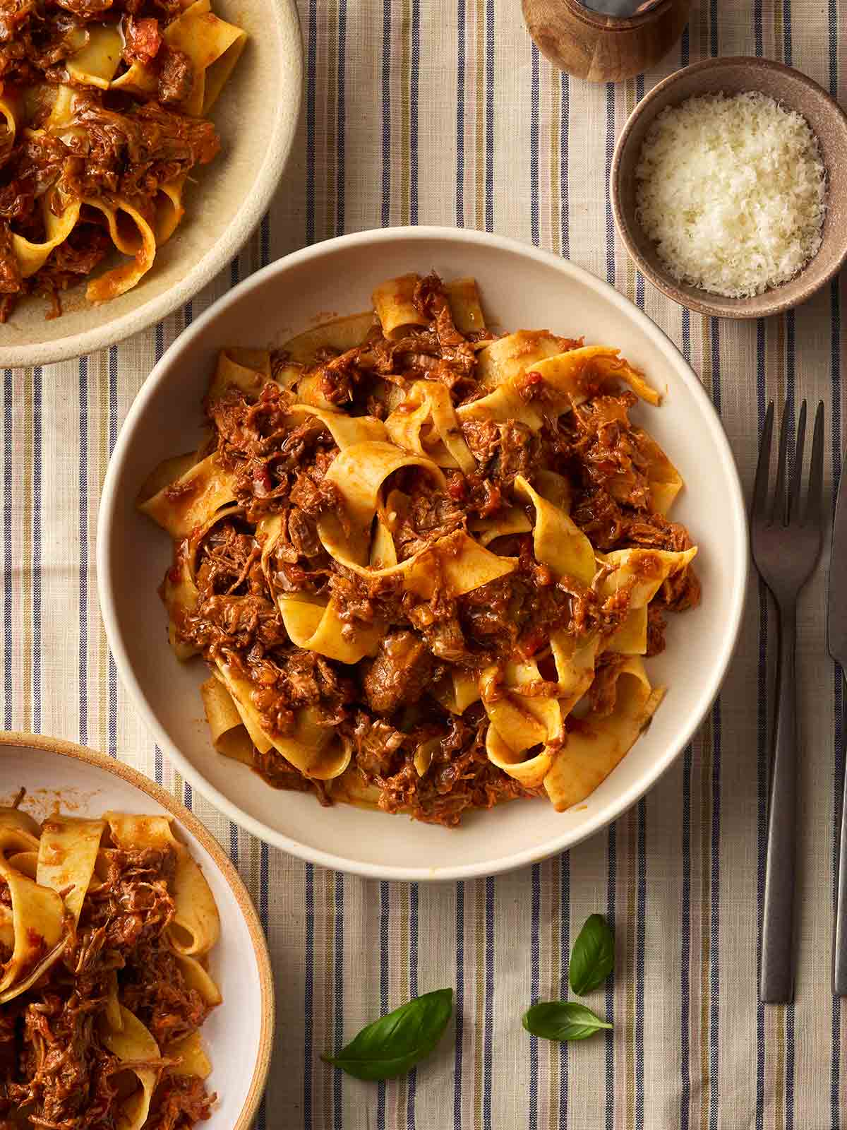 Bowls of Beef Ragu with pappardelle on a table with parmesan in a bowl to the side.