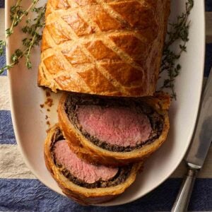 A Beef Wellington served on a platter, with two slices revealing the filling of pink beef and mushroom duxelles.